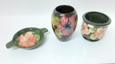 Lot 1228 - Moorcroft pottery vase decorated in the Hibiscus pattern on brown ground, 17.5cm high, together with a planter and an ashtray (3)