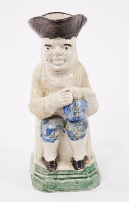 Lot 8 - Creamware Toby jug, circa 1790, shown seated, holding a frothing jug of beer, wearing a cream jacket and blue breeches, on a green square canted base, 16.5cm high