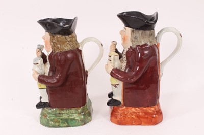 Lot 9 - Two Pearlware Toby jugs, early 19th century, both shown seated, each holding glass of beer in one hand and frothing jug of beer in the other, with red jackets, patterned shirts and yellow breeches,...
