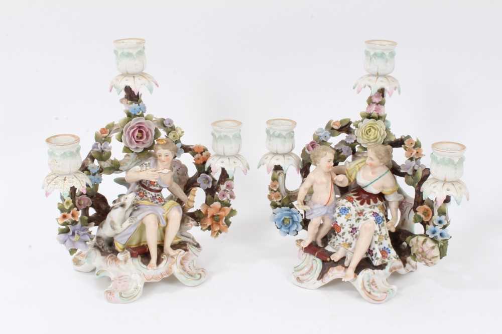 Lot 26 - Pair of Sitzendorf porcelain three-branch figural candelabra, polychrome painted on scrollwork feet, 25cm high