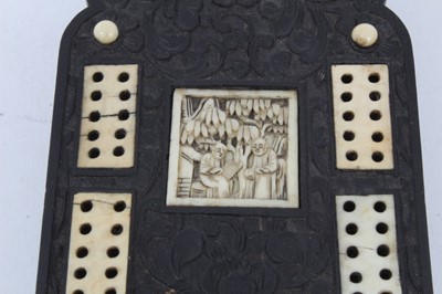 Lot 225 - 19th century Chinese black hardwood cribbage board, with carved floral decoration, inlaid ivory markers and carved plaques with Chinese scenes, slide covered peg box with four pegs, on four carved...