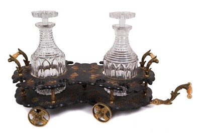 Lot 771 - Regency papier mâché and gilt metal decanter carriage, with pivoting wheels and ivory handle, housing twin cut glass decanters and stoppers, 58cm long