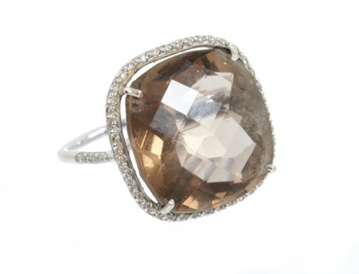 Lot 442 - Smokey quartz and diamond ring with a large cushion shape fancy cut smokey quartz measuring approximately 19.8mm square x 11.5mm, surrounded by a border of brilliant cut diamonds in 18ct white gold...