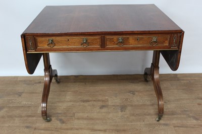 Lot 1457 - Good Regency rosewood and brass mounted sofa table, with rounded rectangular drop leaf top and two frieze drawers, each with lion mask handles  raised on standard ends and splayed legs terminating...