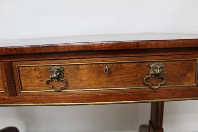 Lot 1457 - Good Regency rosewood and brass mounted sofa table, with rounded rectangular drop leaf top and two frieze drawers, each with lion mask handles  raised on standard ends and splayed legs terminating...