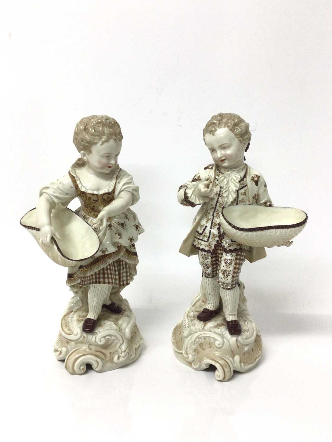 Lot 8 - Pair of continental porcelain figures of a boy and girl, shown holding baskets, on scrollwork bases, with gilt and enamelled decoration, marked to bases, 29cm high