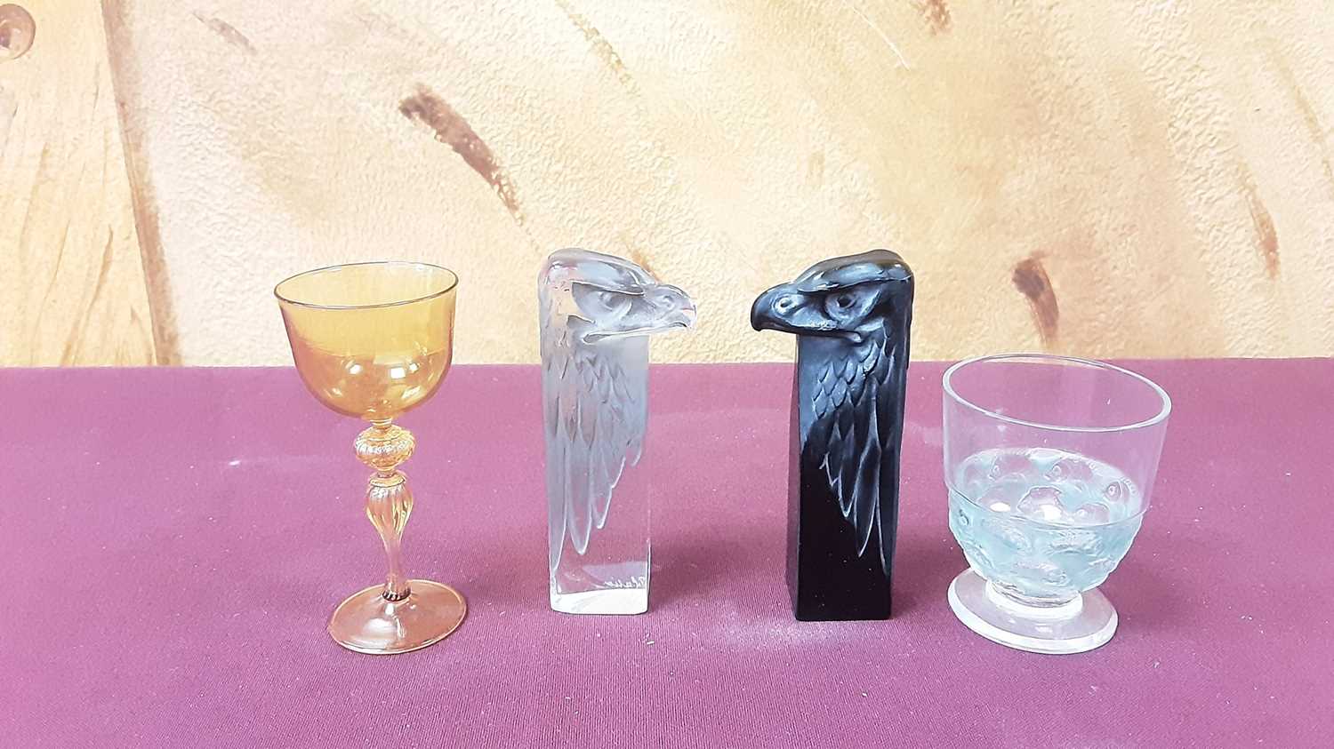 Lot 1022 - Two Lalique glass Eagle heads, 8cm high, together with a small Lalique opalescent drinking glass and an Amber drinking glass (4)