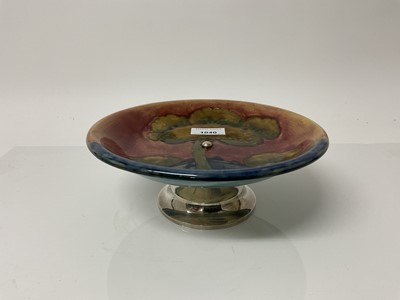 Lot 1040 - Moorcroft pottery flambe Tazza decorated in the Eventide pattern on blue and red ground, on hallmarked silver base, impressed marks and blue painted signature, 8.5cm high, 21.5cm diameter