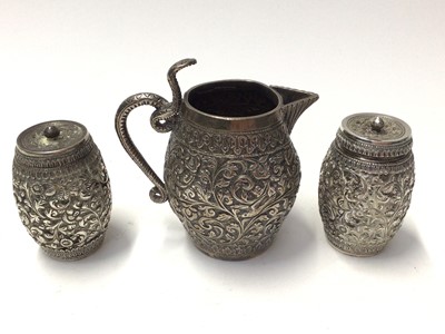Lot 132 - Eastern white metal cream jug with floral scroll and bird decoration, together with similar pair of pepperettes