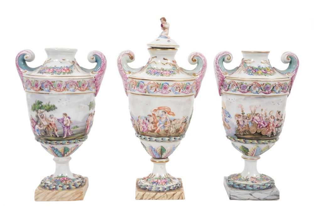 Lot 179 - 19th century Naples porcelain garniture of three classical vases with ornate moulded and polychrome decorated classical figures, one with cover 24-29 cm high