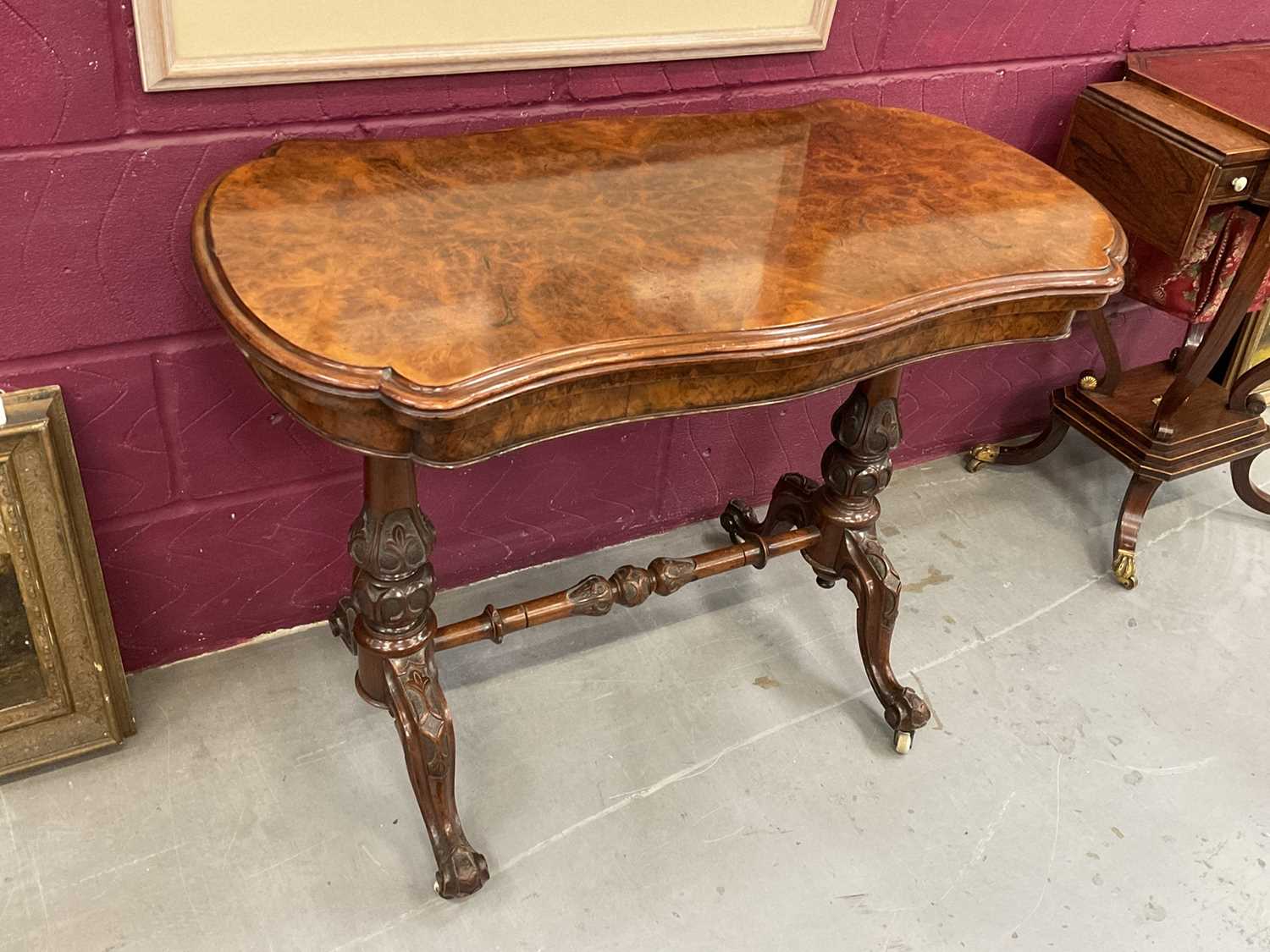 Lot 1213 - Victorian burr walnut veneered card table with shaped fold-over top on carved and turned supports with turned stretcher on cabriole legs terminating on original ceramic casters