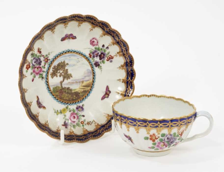 Lot 50 - A Worcester porcelain fluted tea cup and saucer, circa 1780, of Dalhousie type, each painted with a landscape panel on a ground of floral sprays and insects within blue borders highlighted in gilt,...