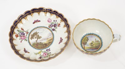 Lot 50 - A Worcester porcelain fluted tea cup and saucer, circa 1780, of Dalhousie type, each painted with a landscape panel on a ground of floral sprays and insects within blue borders highlighted in gilt,...