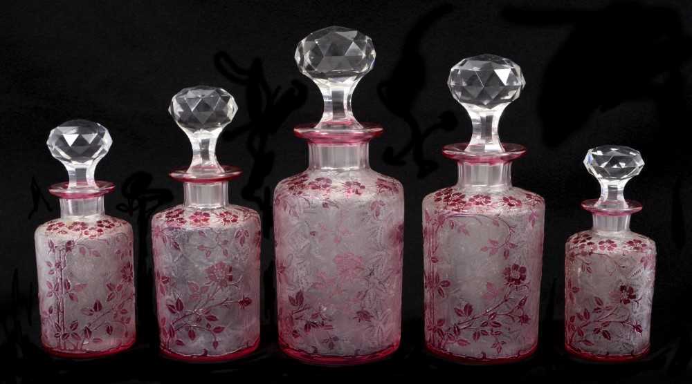 Lot 87 - Rare set of five early 20th century Baccarat crystal graduated scent bottles with facet cut stoppers and cylinderical body with cranberry overlaid faux cameo glass decoration depicting rose bushes...