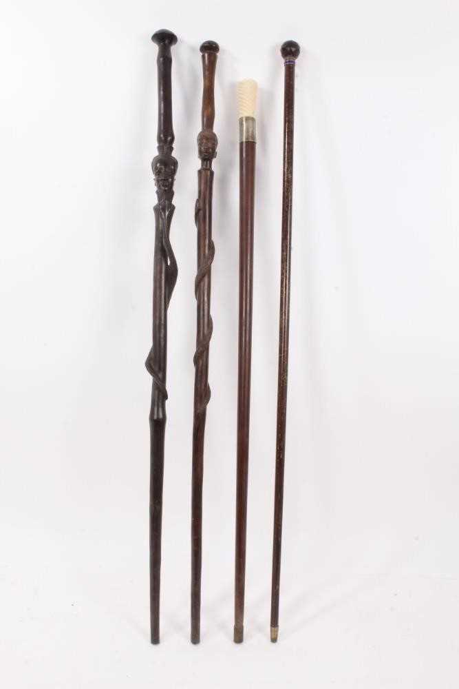 Lot 1017 - Edwardian walking stick with amethyst glass knop, ivory handled cane and two African hardwood canes with African head and snake decoration (4)