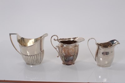 Lot 31 - George V silver cream jug of helmet form with fluted decoration, (Birmingham 1922) together with two Edwardian silver cream jugs (Sheffield 1904) and (Chester 1909), the largest 10cm in height, all...