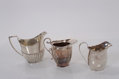 Lot 31 - George V silver cream jug of helmet form with fluted decoration, (Birmingham 1922) together with two Edwardian silver cream jugs (Sheffield 1904) and (Chester 1909), the largest 10cm in height, all...