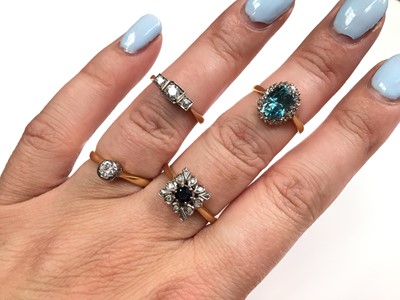 Lot 109 - Four 18ct gold rings to include a three stone diamond ring, single stone diamond ring, blue zircon and diamond cluster ring and a sapphire and diamond cluster ring