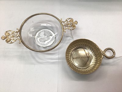 Lot 1077 - Glass dish with silver collar and two cherub handles by William Comyns and plated wine taster (2)