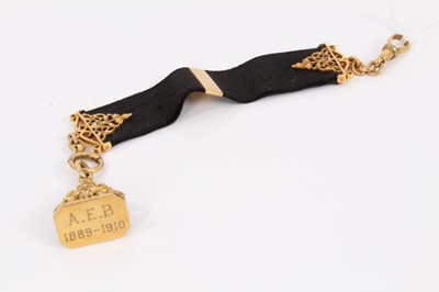 Lot 727 - Edwardian 9ct gold fob with leaf and scrolls, suspended gold mounted black silk ribbon, London 1909, overall length 18.5cm.