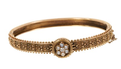 Lot 728 - Victorian Etruscan Revival gold bangle with a central diamond and seed pearl cluster and applied filigree and beaded decoration.