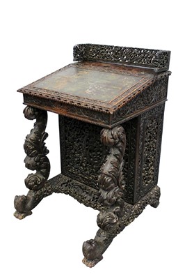 Lot 1505 - 19th century Anglo-Indian carved hardwood davenport desk, with ornate pierced gallery centred by heraldic crest and leather inset sloping fall enclosing short drawers, with door to one side enclosi...