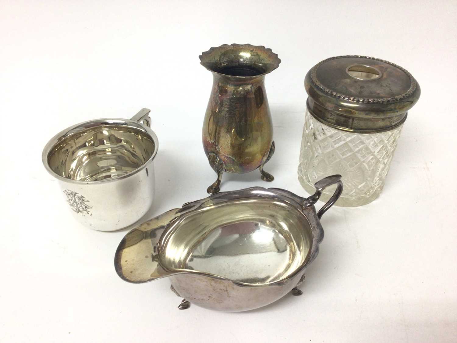 Lot 136 - 1920s silver tea cup with engraved monogram, silver sauce boat, silver vase raised on three legs and silver topped glass jar