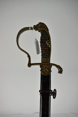 Lot 945 - Imperial German Artillery Officers sabre with brass stirrup hilt, lions head pommel, crossed cannon langet, curved etched blade decorated with military trophies, in black painted steel scabbard