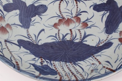 Lot 19 - A 19th century Chinese porcelain charger, painted in underglaze blue and red with lotus flowers