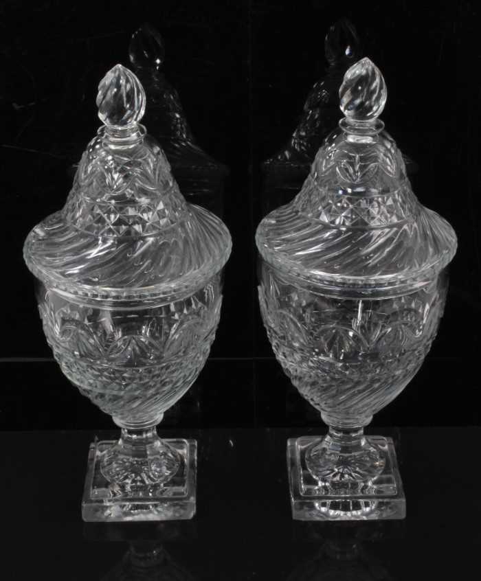 Lot 55 - A pair of Regency cut glass covered urns or bonbonnieres, with bands of fluting, diamond and foliate patterns, on square stepped lemon squeezer bases, 31cm high