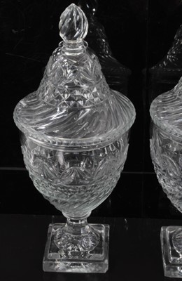 Lot 55 - A pair of Regency cut glass covered urns or bonbonnieres, with bands of fluting, diamond and foliate patterns, on square stepped lemon squeezer bases, 31cm high