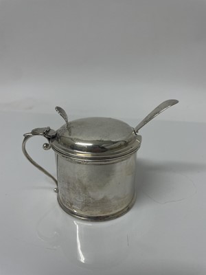 Lot 841 - Edwardian silver drum mustard, with scroll handle and hinged domed cover, with shell thumb piece, blue glass liner (Birmingham 1907). Deakin & Francis. Together with a Georgian silver condiment spo...