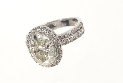 Lot 408 - Diamond halo cluster ring with an oval mixed-cut diamond weighing approximately 3cts, surrounded by a border of round brilliant cut diamonds with diamond set shoulders on a white gold shank.