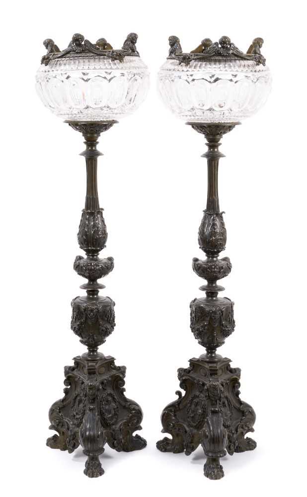 Lot 1453 - Pair of 19th century bronze candlesticks converted for electricity, each with inverted cut glass bowls, raised on flared column with mask swag and stiff leaf ornament, 71cm