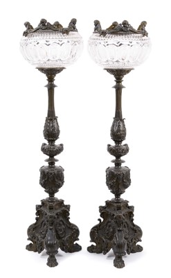 Lot 1453 - Pair of 19th century bronze candlesticks converted for electricity, each with inverted cut glass bowls, raised on flared column with mask swag and stiff leaf ornament, 71cm