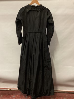 Lot 2065 - Victorian black dress with flat front opening, pleated skirt with buttoned hem and leg of mutton sleeve.  Plus a long black evening jacket, black applique silk edged in chain stitch on black net la...