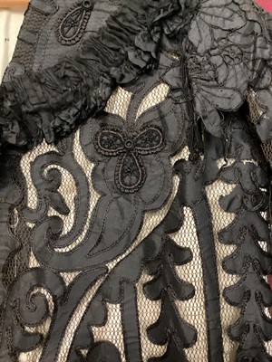 Lot 2065 - Victorian black dress with flat front opening, pleated skirt with buttoned hem and leg of mutton sleeve.  Plus a long black evening jacket, black applique silk edged in chain stitch on black net la...