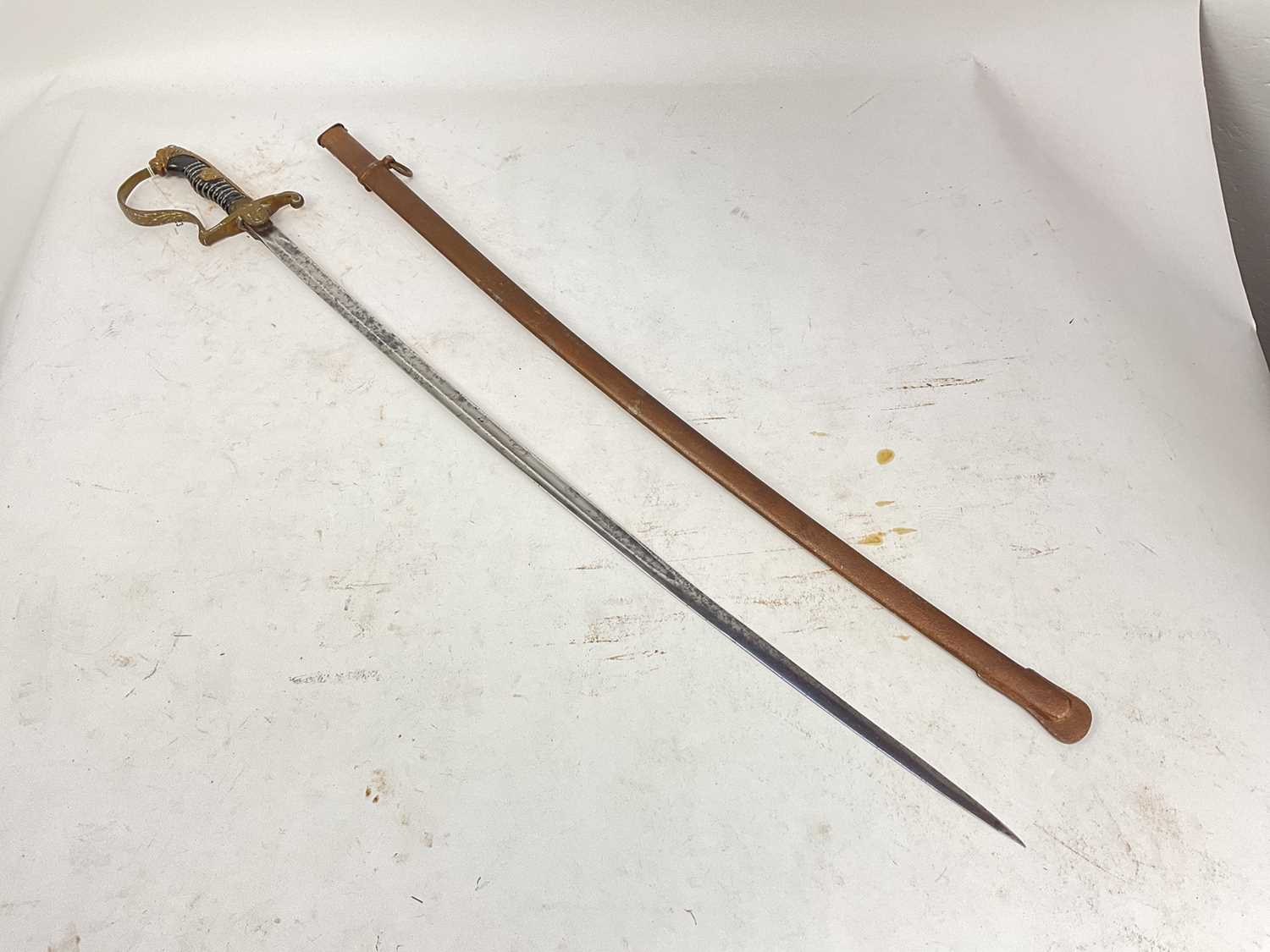 Lot 823 - Nazi Cavalry Officer's sword with brass lions head pommel and glass eyes, stirrup hilt with eagle and swastika langet, plain fullered blade in scabbard