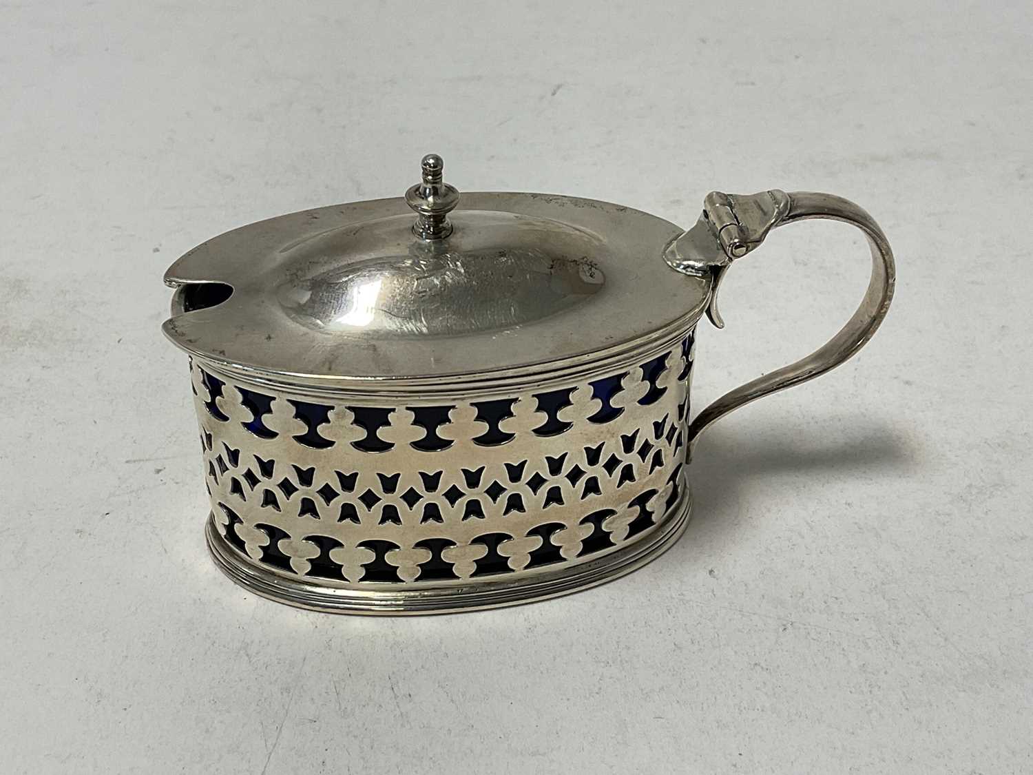 Lot 124 - Edwardian silver mustard pot of oval form, with pierced decoration and blue glass liner, (London 1906), 9.5cm in length.