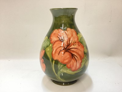 Lot 1250 - Moorcroft pottery vase decorated in the Hibiscus pattern on green ground, impressed marks to base, and original paper label - Potters To The Late Queen Mary, 21.5cm high