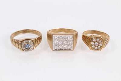 Lot 906 - Two 9ct gold rings set with synthetic white stones and one other 9ct gold blue stone ring, all with textured shoulders on 9ct yellow gold shanks (3)