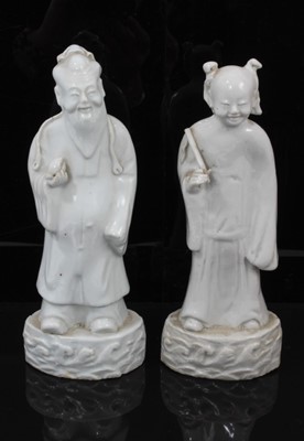Lot 38 - Pair of Chinese Qing period blanc de chine figures, the female figure carrying a fly whisk, the male figure carrying a piece of fruit, both standing on bases with stylised waves, 21.5cm and 22cm hi...
