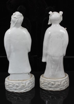 Lot 38 - Pair of Chinese Qing period blanc de chine figures, the female figure carrying a fly whisk, the male figure carrying a piece of fruit, both standing on bases with stylised waves, 21.5cm and 22cm hi...