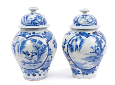 Lot 76 - A pair of 18th/19th century Japanese blue and white baluster vases and covers, painted with panels containing landscape scenes on a floral decorated ground, six-character marks, 32.5cm total height