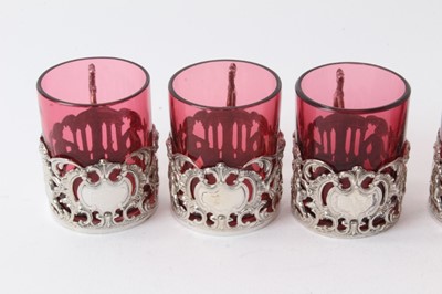 Lot 225 - Set six Edwardian silver mounted ruby glass beakers with rococo and cherub decoration, (Chester 1906), 6cm high