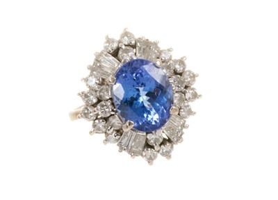 Lot 439 - Tanzanite and diamond cluster cocktail ring with an oval mixed cut blue sapphire measuring approximately 10.1mm x 8.1mm x 5.6mm surrounded by brilliant cut and tapered baguette cut diamonds in claw...