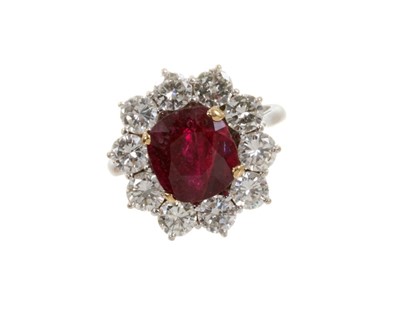 Lot 450 - Ruby and diamond cluster ring with an oval mixed cut ruby measuring approximately 9.1mm x 8.3mm x 6.1mm surrounded by a border of ten brilliant cut diamonds in claw setting on 18ct white gold shank...