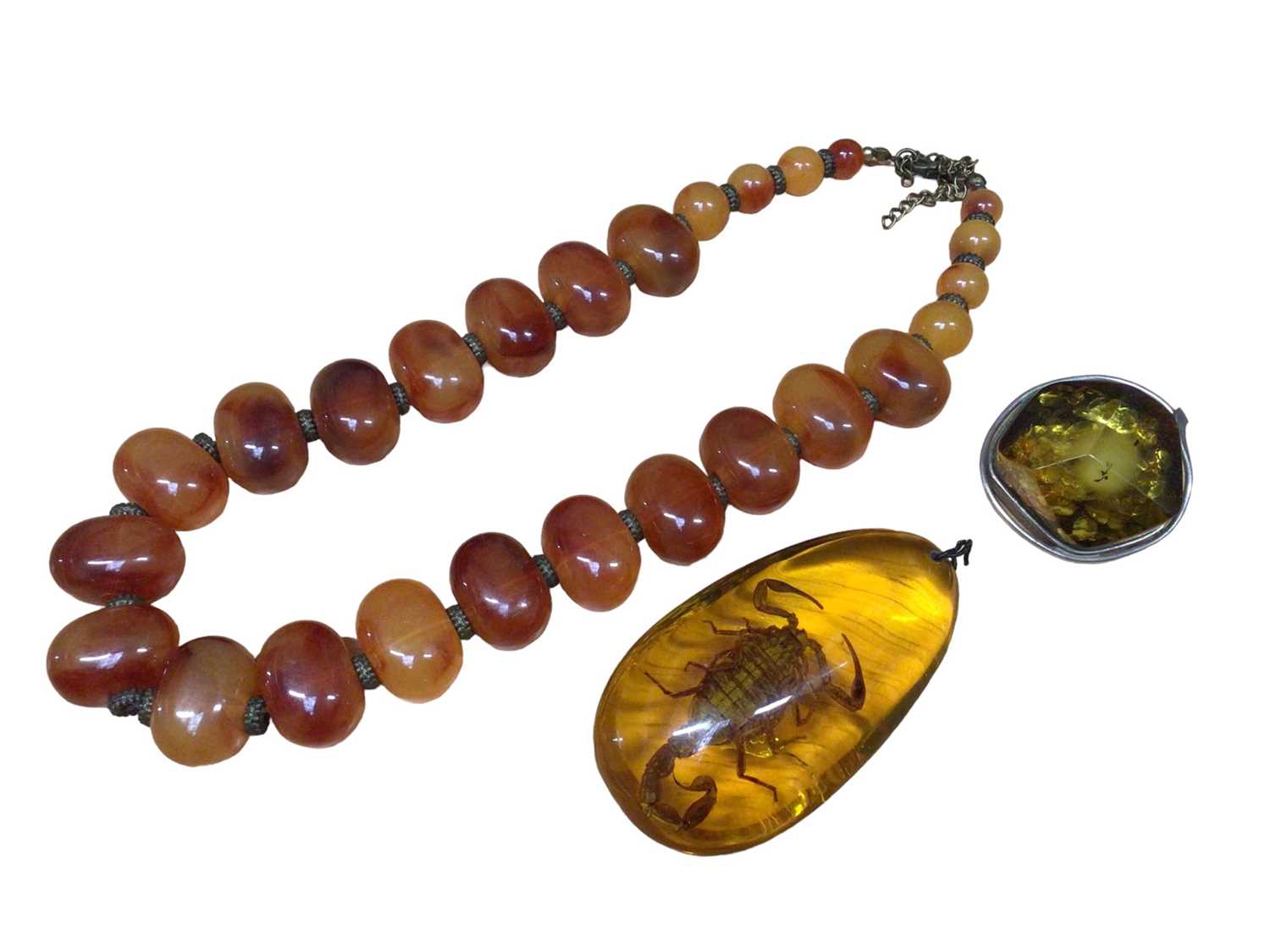 Lot 112 - Large reconstituted amber pendant with a scorpion inside, reconstituted amber brooch in white metal mount and a plastic bead necklace