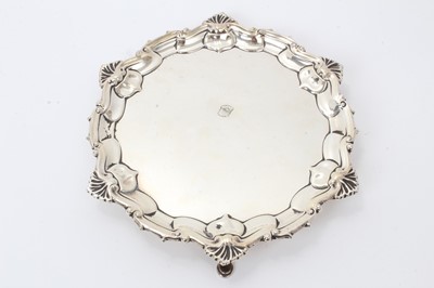 Lot 548 - 1920s silver waiter of circular form with shell and scroll border, on three hoof feet