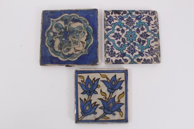 Lot 383 - Three Persian tin-glazed pottery tiles, each decorated with foliate patterns, the largest 11cm x 11cm